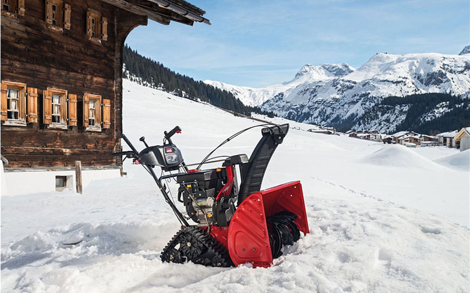 Schneefräse im Einsatz vor einer verschneiten Alpenkulisse